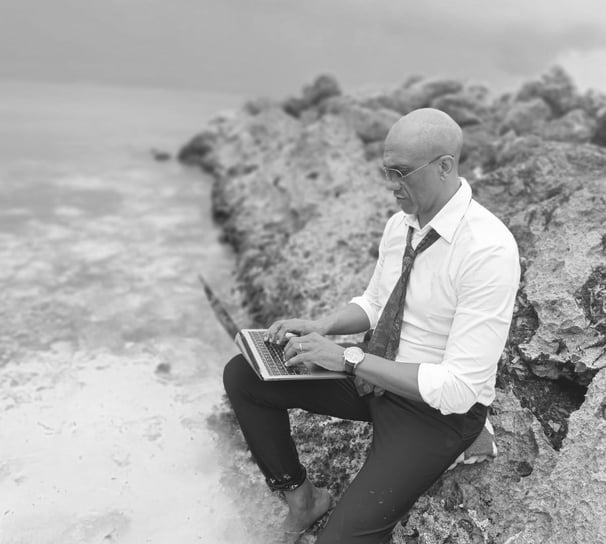 « Bruno Valery travaillant sur son ordinateur, assis sur un rocher les pieds dans l’eau en Guadeloupe »