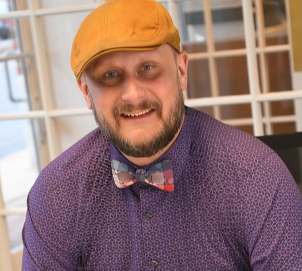 a portrait of Andy Albright wearing a yellow hat and purple shirt