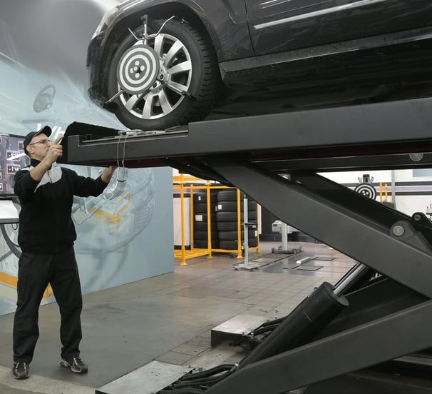 a man standing on a lift with a car on the lift trying to align its frame at fix collision center