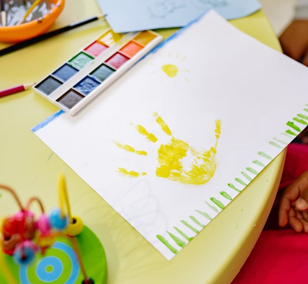 Dessin bébé avec empreinte main jaune sur table avec jouets - Micro-crèche def