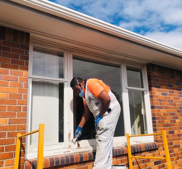 a man in a orange shirt and white pants is painting a window