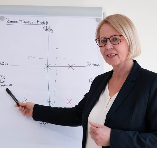 a woman in a business suit is holding a pen and pointing at a white board