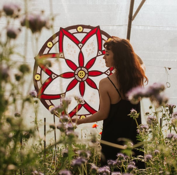 Artiste tenant son oeuvre dans ses bras. Rosace en vitrail écologique au milieu de fleurs sauvages