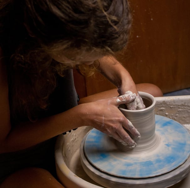 A person leaning over a piece while throwing on a potter's wheel.