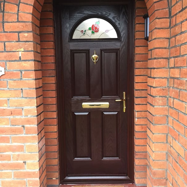 Rosewood front door with rose pattern glass and gold hardware on a red brick house