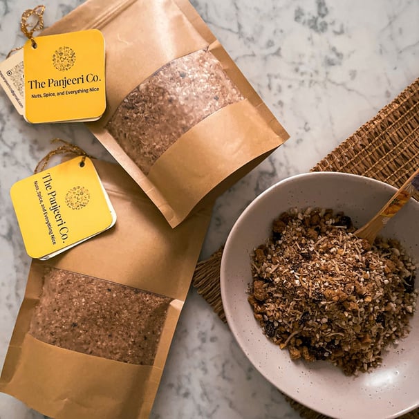 Chocolate Panjeeri/ granola served in a bowl alongside sealed, recyclable brown paper bags