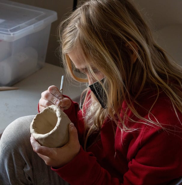 Young girl using a pencil tool to carve into a small ceramic cup.