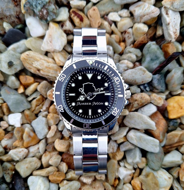 Amser Mon Anglesey black and white metal watch on pebbles on a beach