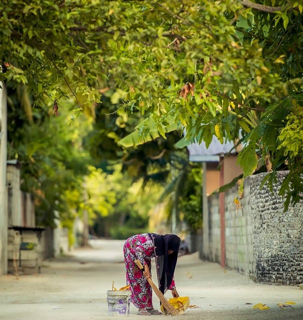 a woman in a pink dress is cleaning a sidewalk