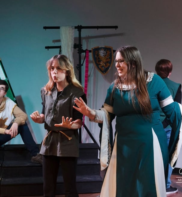 a teen actor playing Guinevere in Camelot in a green dress standing in front of a stage
