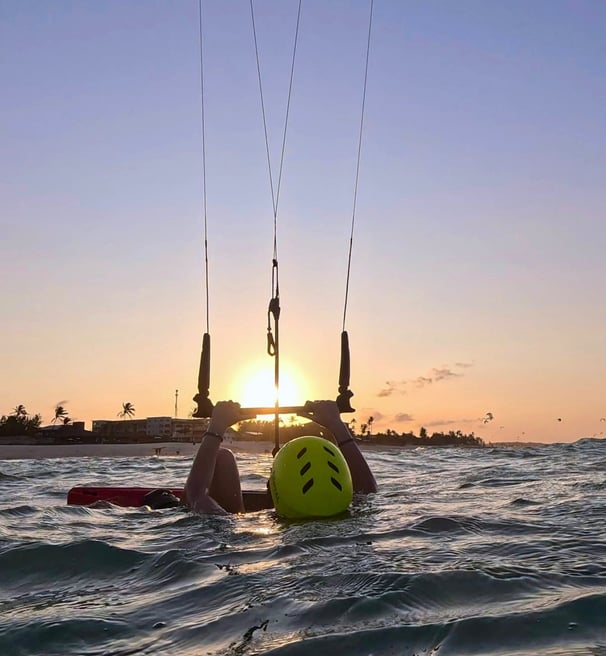 mulher dentro da água segurando o kite e vendo o por do sol.