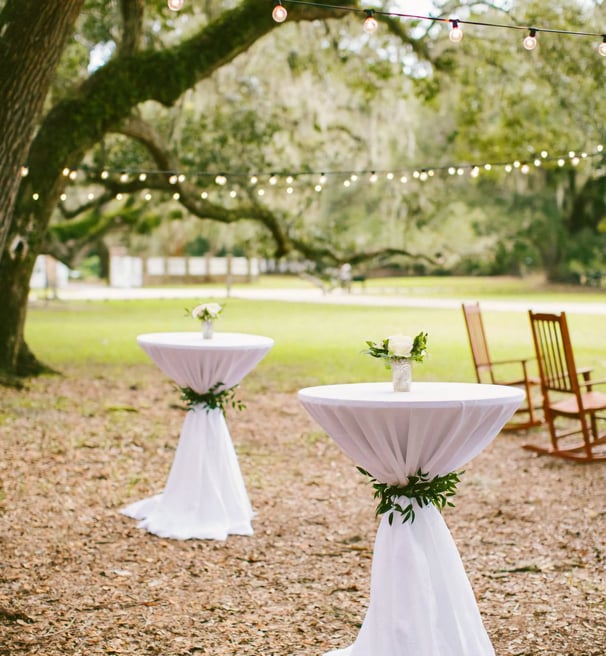 Mesa de coctel decorada para boda al aire libre, con mantel y decorascion floral
