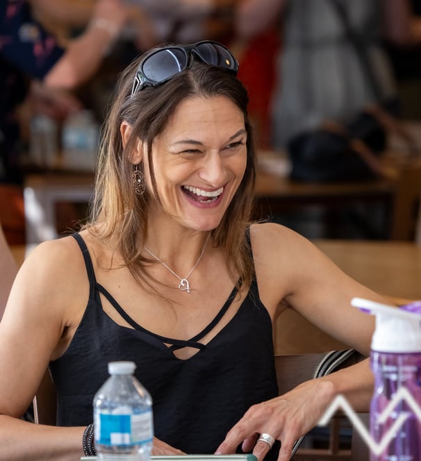 Lady laughing sitting at a table she has sunglasses on her head