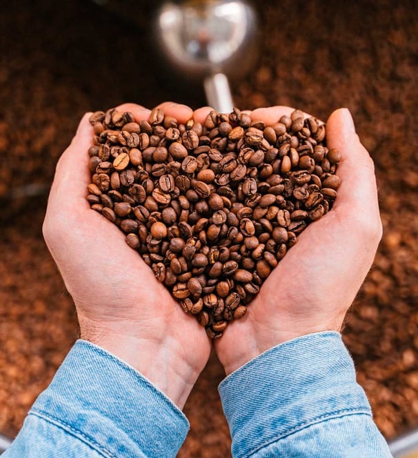Hand forming a heart with Colombian coffee beans, symbolizing passion and care