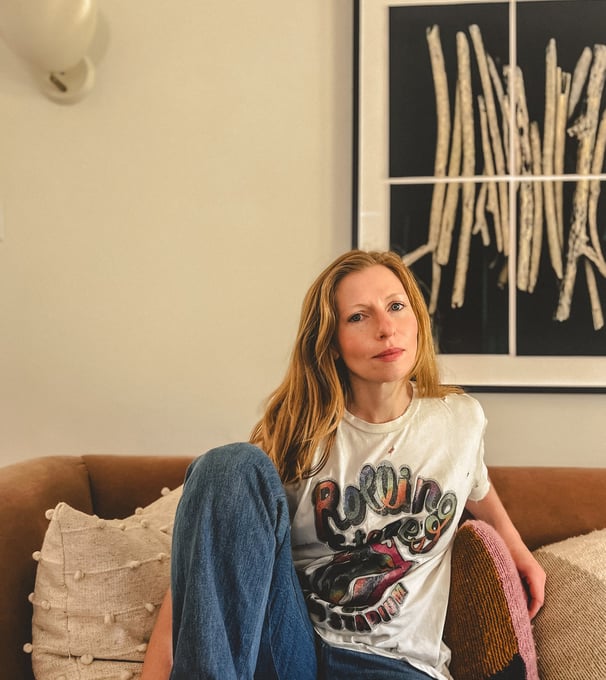 Editorial portrait of a yoga teacher with red hair and somatic practitioner, seated on a sofa. 