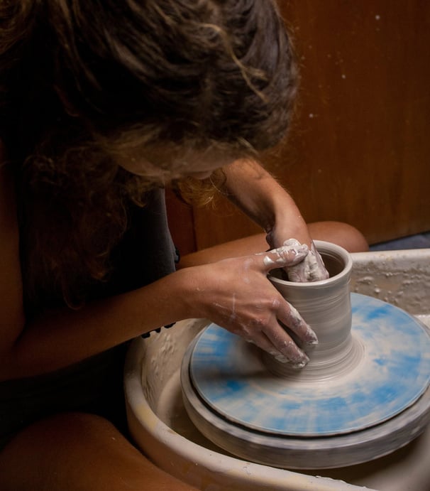 A person leaning over a piece while throwing on a potter's wheel.