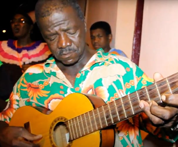 Sr. João tocando violão, símbolo da música e tradição oral de São Tomé