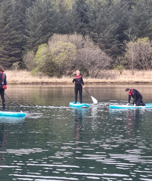 2 paddle board students and SUP coach on a calm lake.