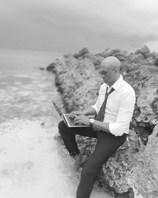« Bruno Valery travaillant sur son ordinateur, assis sur un rocher les pieds dans l’eau en Guadeloupe »