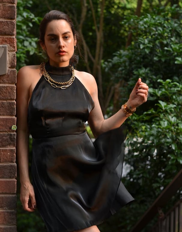 Cynthia Scellos in a black dress standing on a brick wall