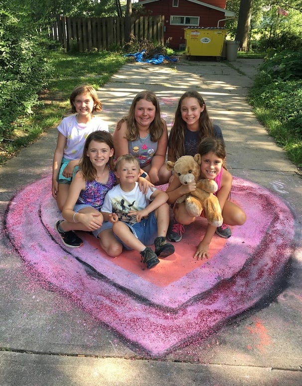 Group of smiling children posing on top of a large chalk heart they made.