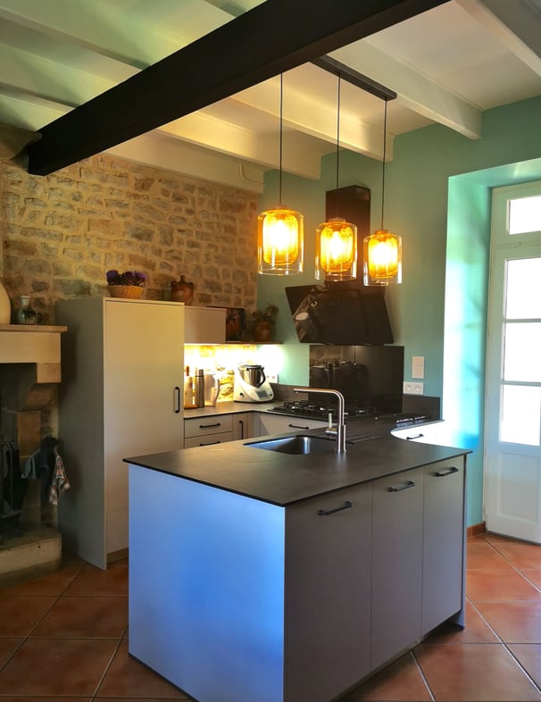 Cuisine beige, plan de travail en ardoise, cuve inox et robinetterie inox brossée. Hotte murale noir