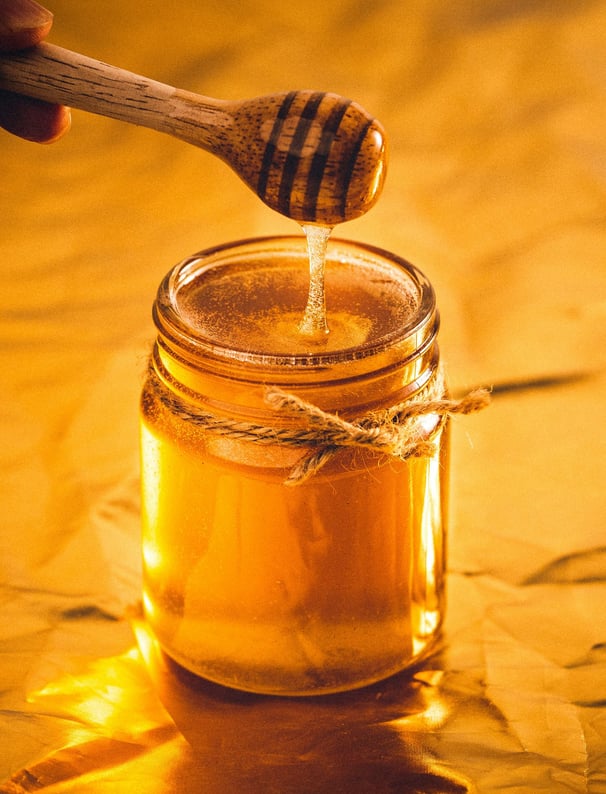 Jar of golden honey with a honey dipper dripping honey, set against a warm background.