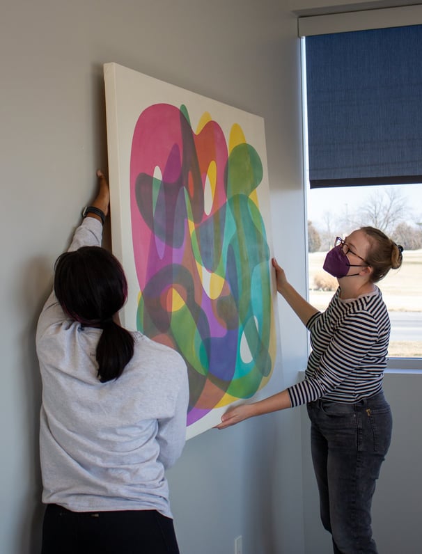 Two individuals hanging a colorful painting on one of our walls.