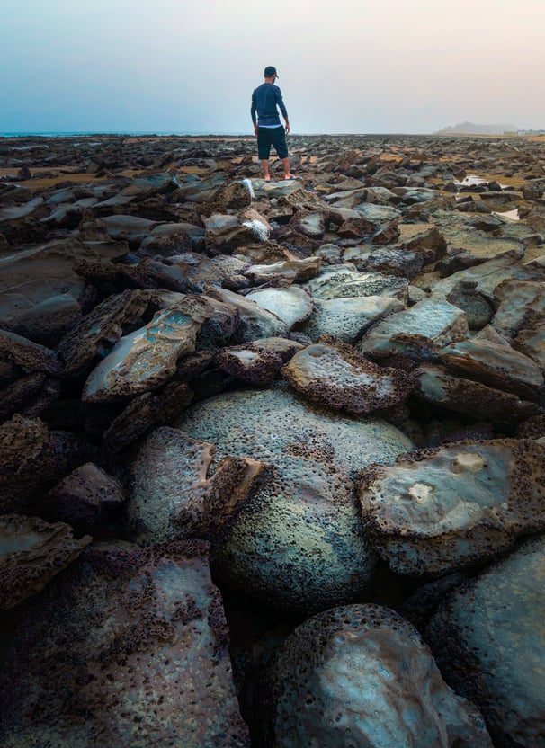 a man standing on a rocky beach with a surfboard