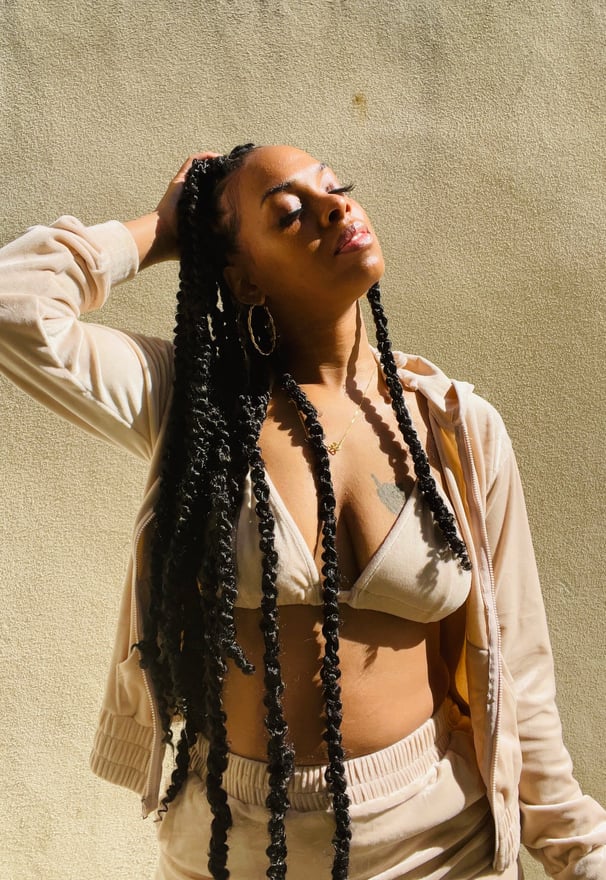 A confident Black woman with long twists in a beige loungewear set,