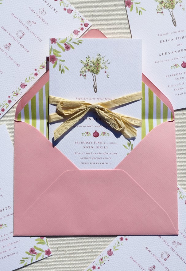 close up of invitation with pomegranate tree inside of pink envelope with stripped green lining