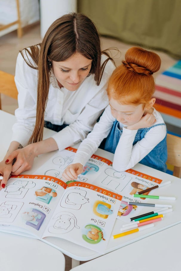 A young girl reading a children's picture book with a teacher.