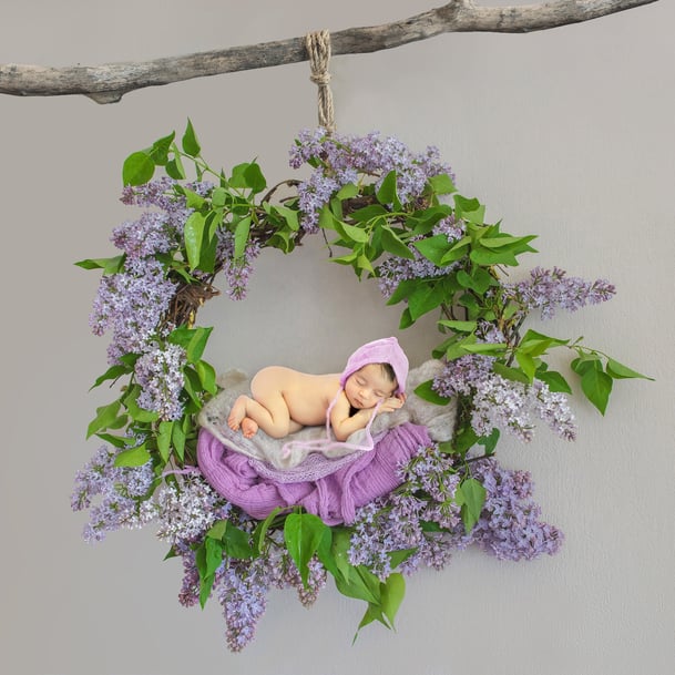 newborn baby girl sleeping on a floral ring wearing pink and purple soft wool beanie bonnet hanging from a tree branch