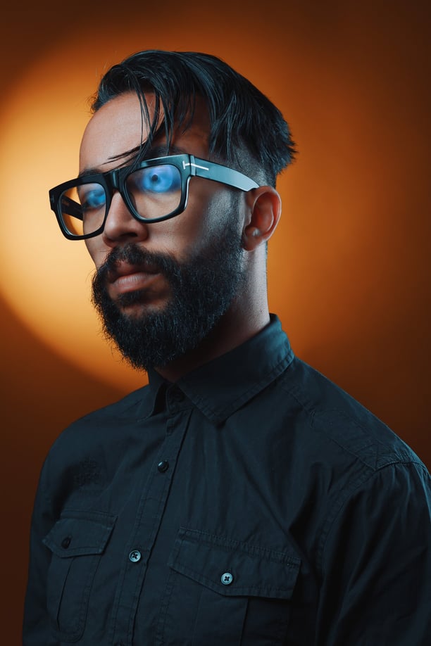 Un homme barbu avec des lunettes posant devant un fond orange.