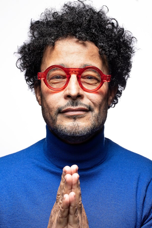 Un homme aux cheveux bouclés portant des lunettes rouges.