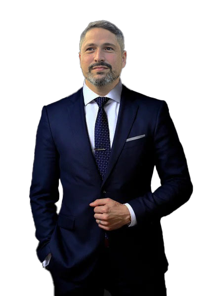 Homem branco de barba grisalha sorrindo vestindo terno e com gravata azul marinho