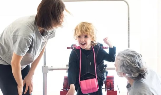 Dos personas adultas ayudando a un niño con paralisis cerebral con fisioterapia