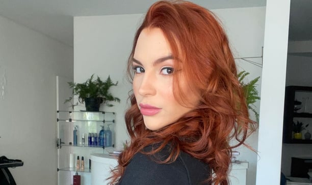 Mulher ruiva, cabelos ondulados com olhar profundo.