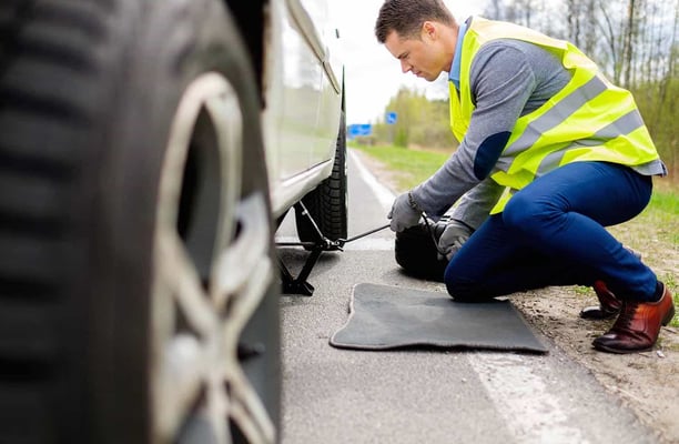 a man in a yellow vest is fixing a tire on a car