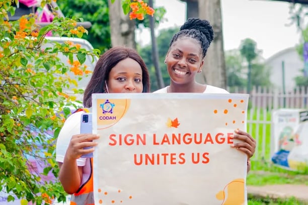 2 women smiling while holding a banner that says "Sign language unites us"
