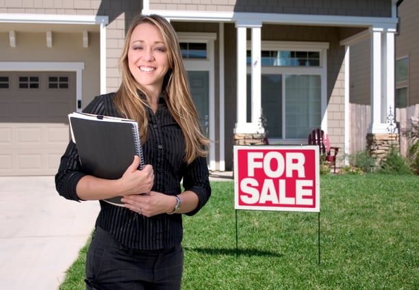 A happy Realtor standing in front of a home she just listed for sale