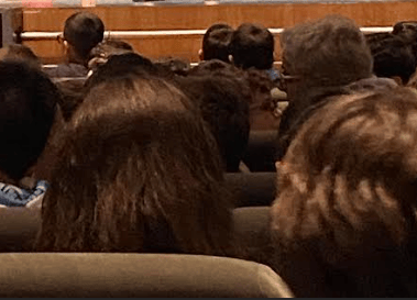 a man in a suit and tie is standing in front of a lecture hall