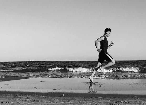 a man running on the beach with a surfboard