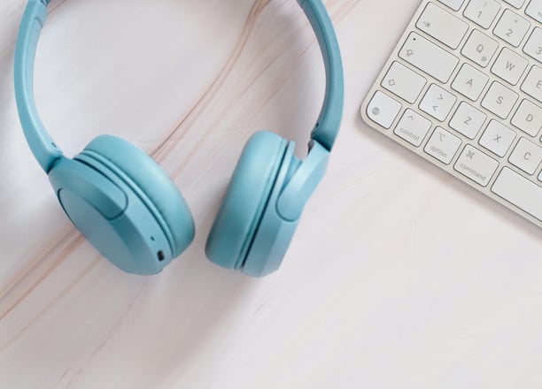 Blue wireless headphones and a white keyboard on a clean desk, symbolizing online learning, language