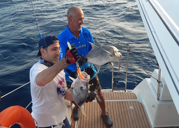 Anglers proudly showing their caught Giant Trevally on a catamaran - Catamaran Fishing Charters