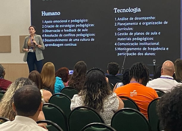 Jailana palestrando em um auditório, com um slide projetado que compara aspectos "Humano" e IA