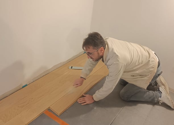 Un artisan qui pose du parquet flottant en bois.