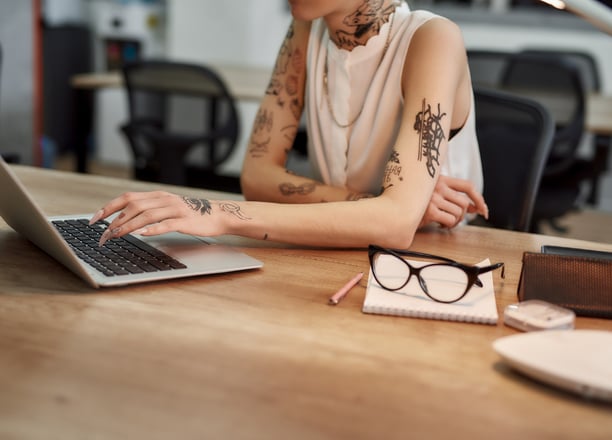 tattooed woman scrolling laptop