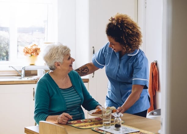Compassionate caregiver assisting an elderly client with a meal at home, personalized home care