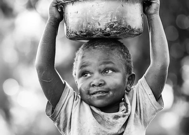 A smiling African child carrying a water container